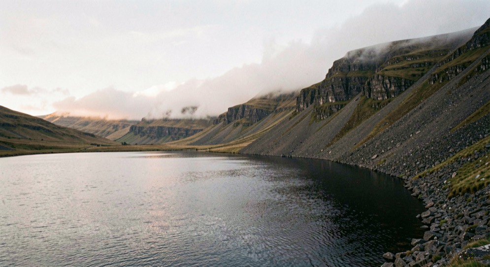 Dawn over Wast Water in the Lake District, black still water across the foreground, the screes falling steeply into the lake on the right, low cloud caught along the ridge, wide horizontal framing